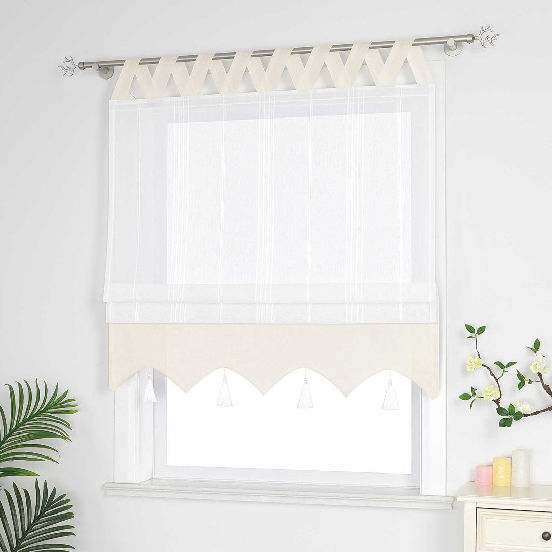 Beige und weisse Raffrollo Gardine mit Schlaufen dekorativen Quasten und geschwungenem Saum halb hochgezogen, Seitenansicht eines weißen Raffrollos mit Quasten und Schlaufen – halb geschlossen, sodass die Fenster nicht vollständig bedeckt sind, neben Grünpflanzen und duftenden Ornamenten.