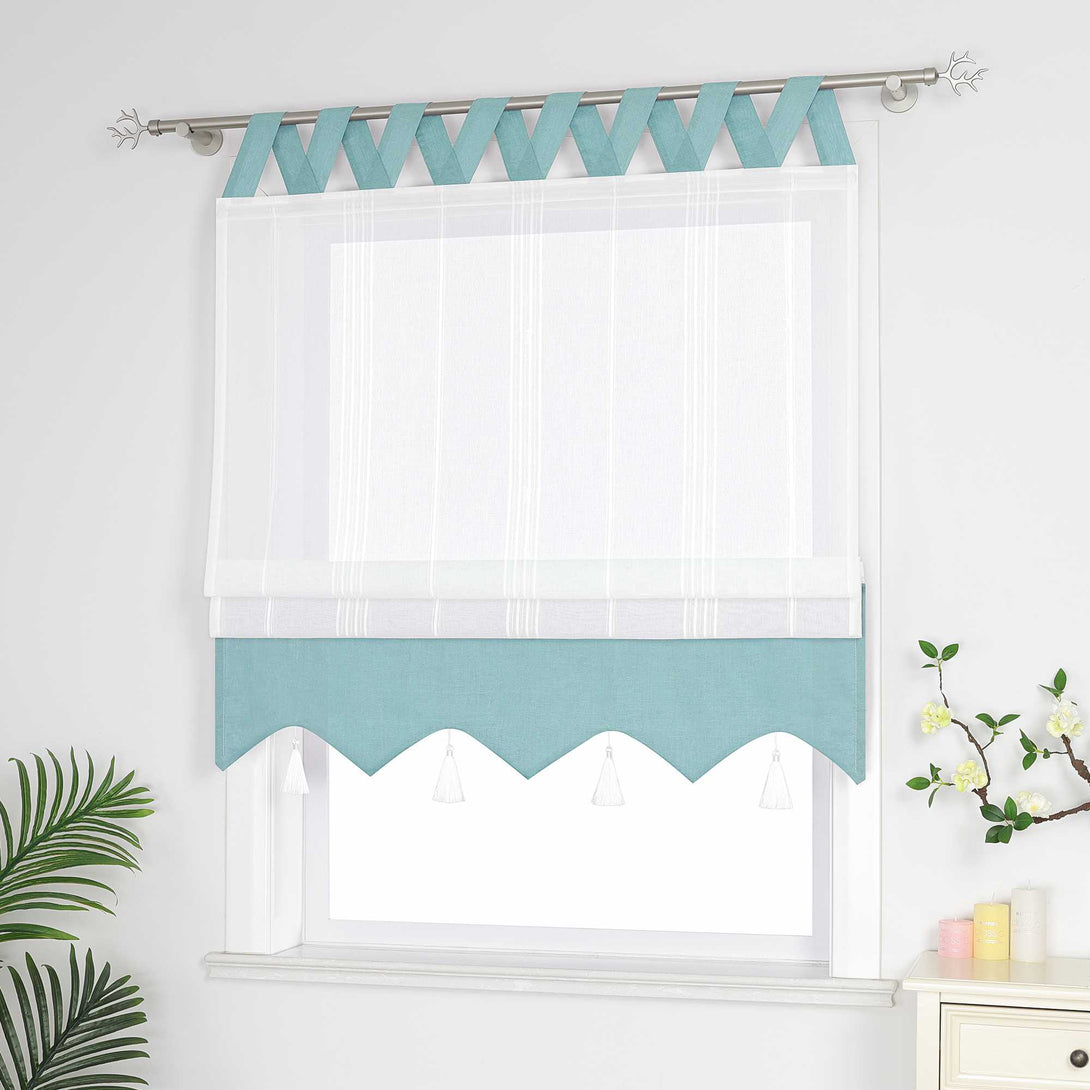 Blaue und weisse Raffrollo Gardine mit Schlaufen dekorativen Quasten und geschwungenem Saum halb hochgezogen, Seitenansicht eines weißen Raffrollos mit Quasten und Schlaufen – halb geschlossen, sodass die Fenster nicht vollständig bedeckt sind, neben Grünpflanzen und duftenden Ornamenten.