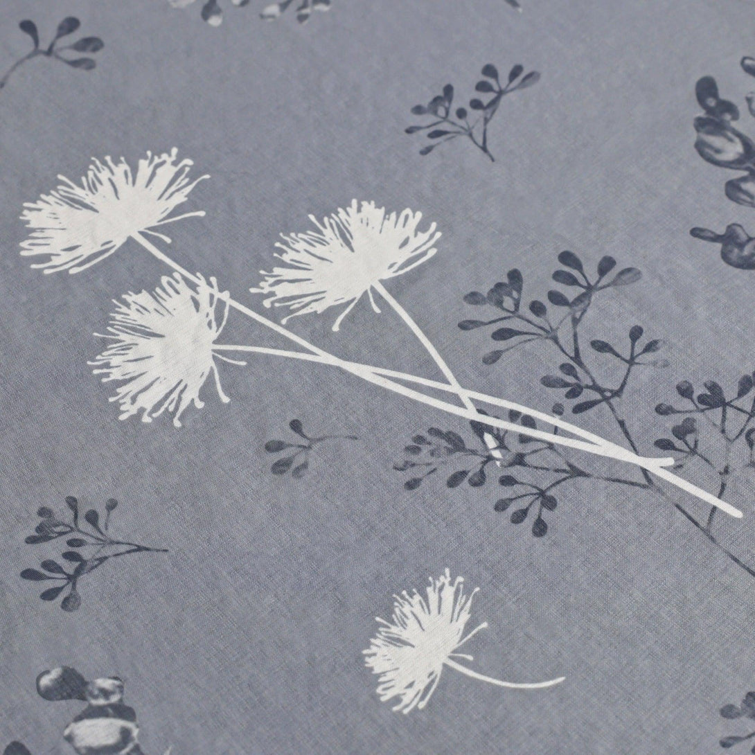 Dies ist eine Nahaufnahme eines Stoffes mit einem grau-blauen Hintergrund, auf dem weiße Dandelion-Blumen und dunkle Zweige und Blätter abgebildet sind. Die feine Textur des Stoffes verleiht ihm eine natürliche und frische Ausstrahlung.
