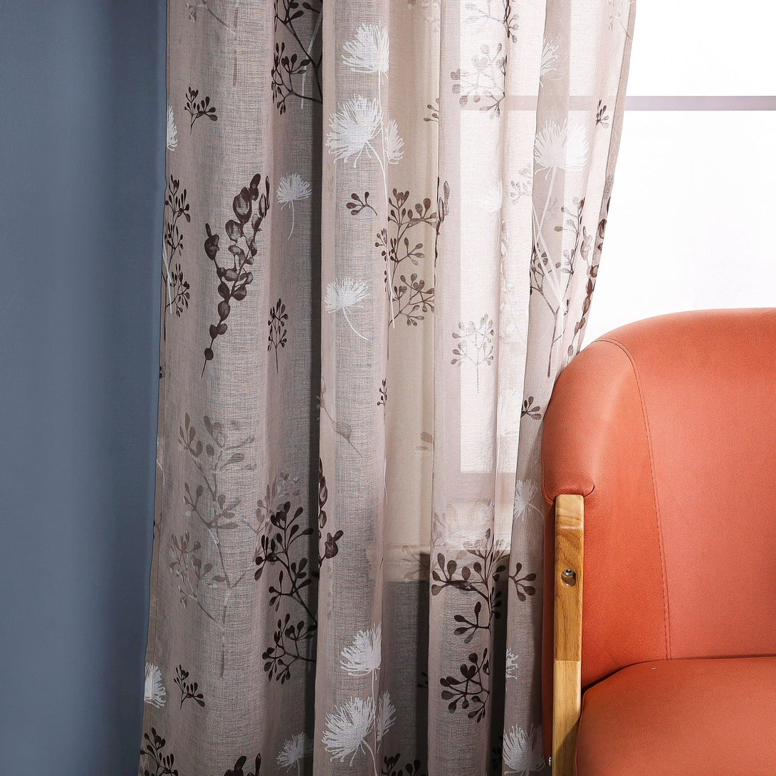 Das Bild zeigt einen transparenten Vorhang mit einem Blumenmuster auf hellem Hintergrund, mit weißen Blumen und tiefbraunen Zweigen und Blättern. Neben dem Vorhang steht ein orangefarbener Stuhl mit Holzbeinen, und im Hintergrund ist eine blaue Wand zu sehen.