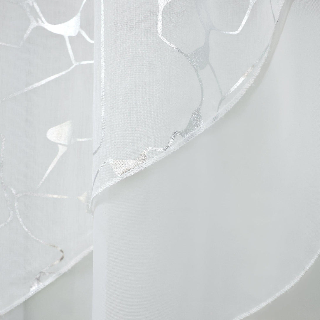 Detailaufnahme der doppelten Küchenvorhänge mit Silberdruck. Sie können sehen, dass die Vorhänge mit einer feinen, unregelmäßigen Struktur bedruckt sind und die beiden Teile getrennt werden können. Die Seite mit silbernem Glitzer auf jedem Stück der Gardine ist kürzer als die schlichte weiße Seite dahinter. Die Umwicklung ist aus weißem Garn.