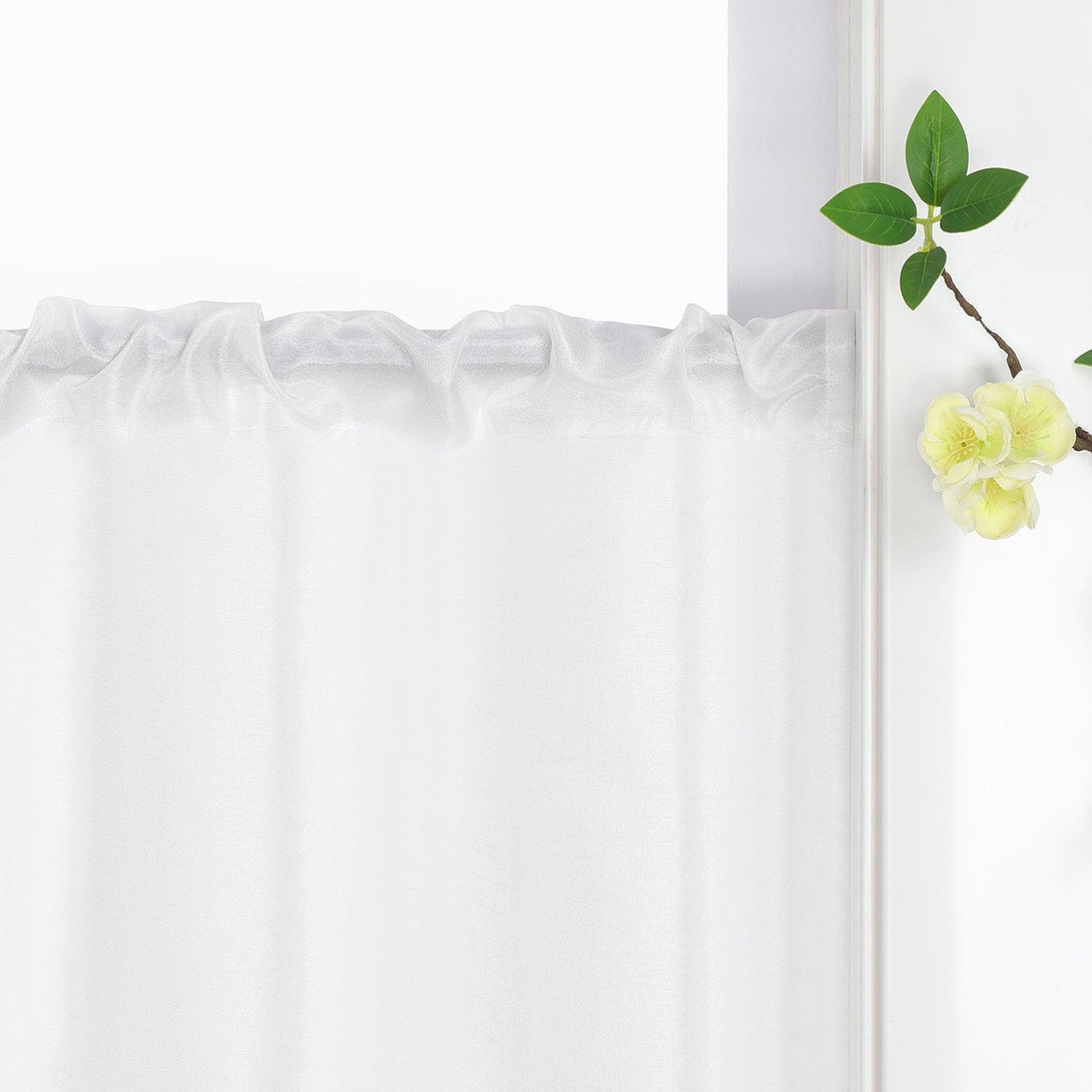 Die weiße Scheibengardine hängt elegant am Vorhangstab. Der Stoff fällt natürlich und gerade, während Blumen als Dekoration daneben platziert sind.