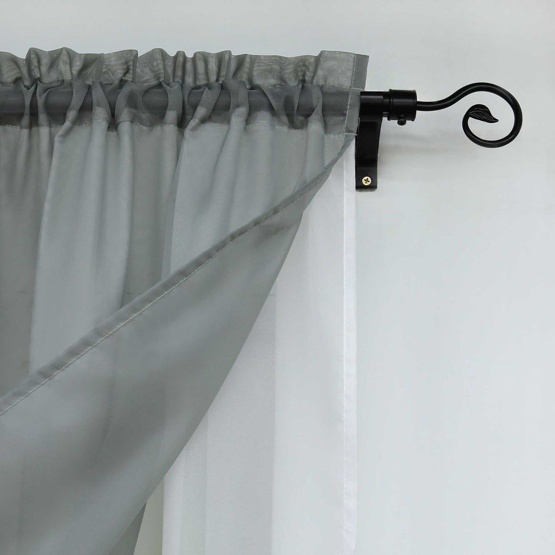 Nahaufnahme der grauen halbtransparenten Gardinen. Der Saum des oberen Teils der Gardinen sorgt für eine gleichmäßige Faltung, während die Gardinen an einer eleganten schwarzen Gardinenstange befestigt sind.