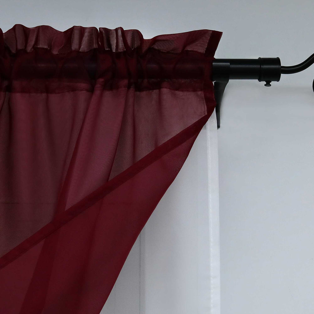 Nahaufnahme der halbdurchsichtigen Gardinen in weinroter Farbe. Der Saum am oberen Teil der Gardinen sorgt für eine gleichmäßige Faltung, während die Gardinen an einer eleganten schwarzen Gardinenstange befestigt sind.
