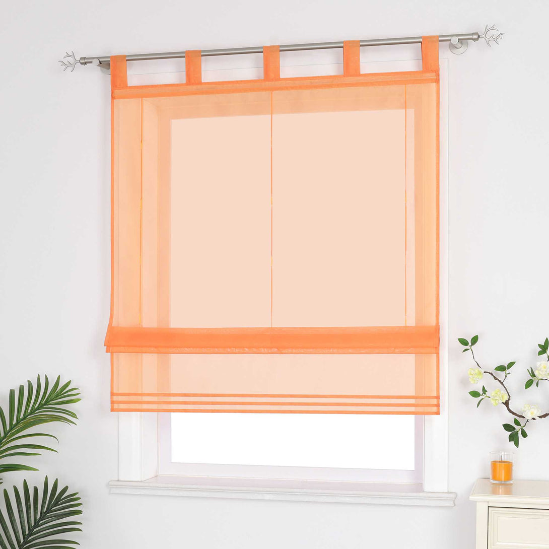 Halbtransparenter oranger Raffrollo hängt vor dem Fenster und sorgt für eine helle, luftige Atmosphäre. Daneben setzen grüne Pflanzen dekorative Akzente. Seitliche Ansicht.
