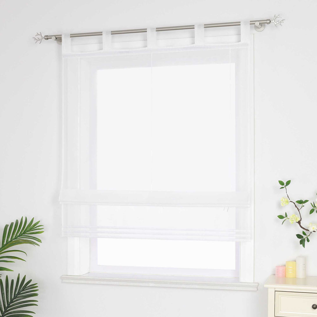 Halbtransparenter weißer Raffrollo hängt vor dem Fenster und sorgt für eine helle, luftige Atmosphäre. Daneben setzen grüne Pflanzen dekorative Akzente. Seitliche Ansicht.