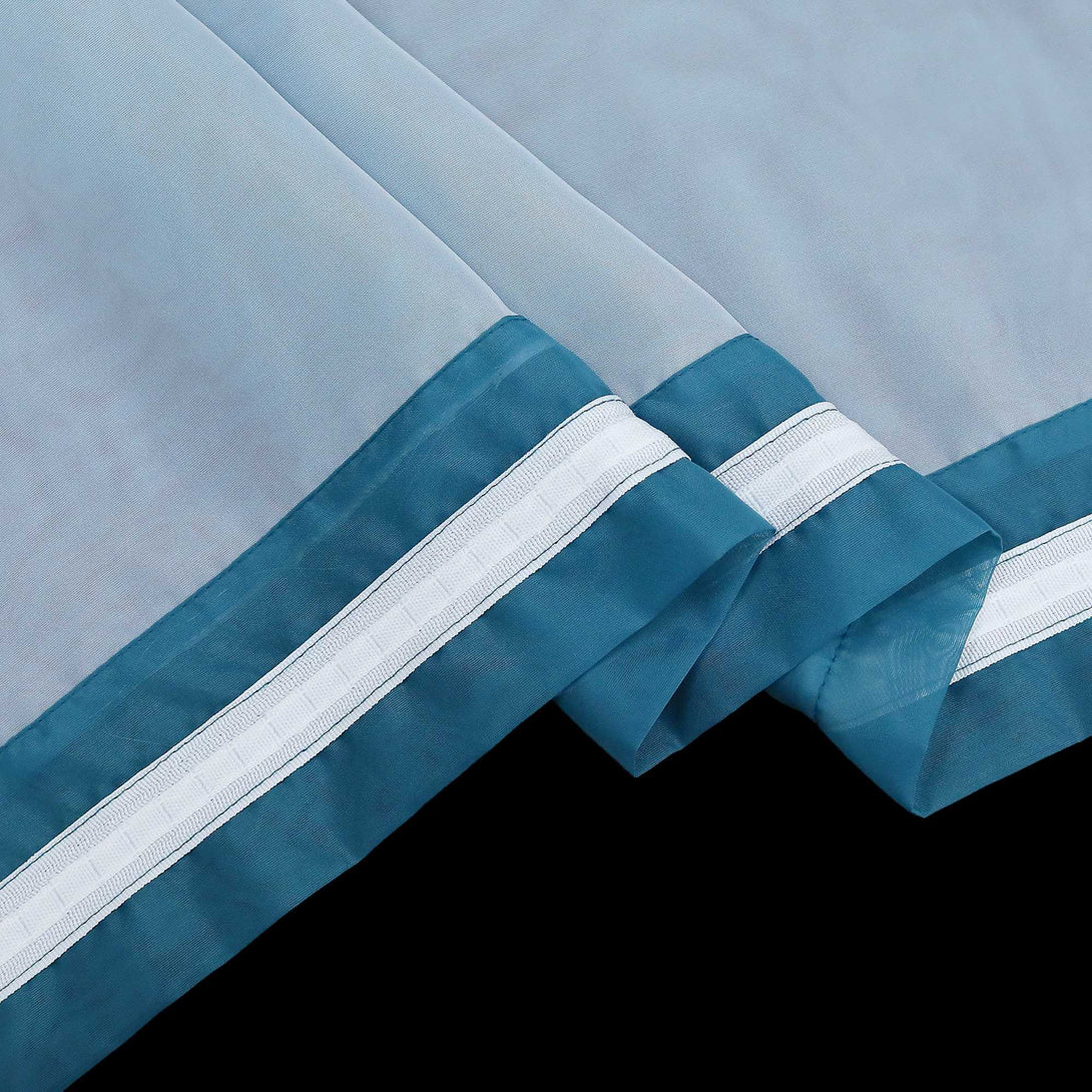 Detail eines blauen halbtransparenten Gardinenstoffs mit deutlich sichtbarem Saum und sauber gefalteten Kanten. der blaue Stoff hat weiße Nähte.