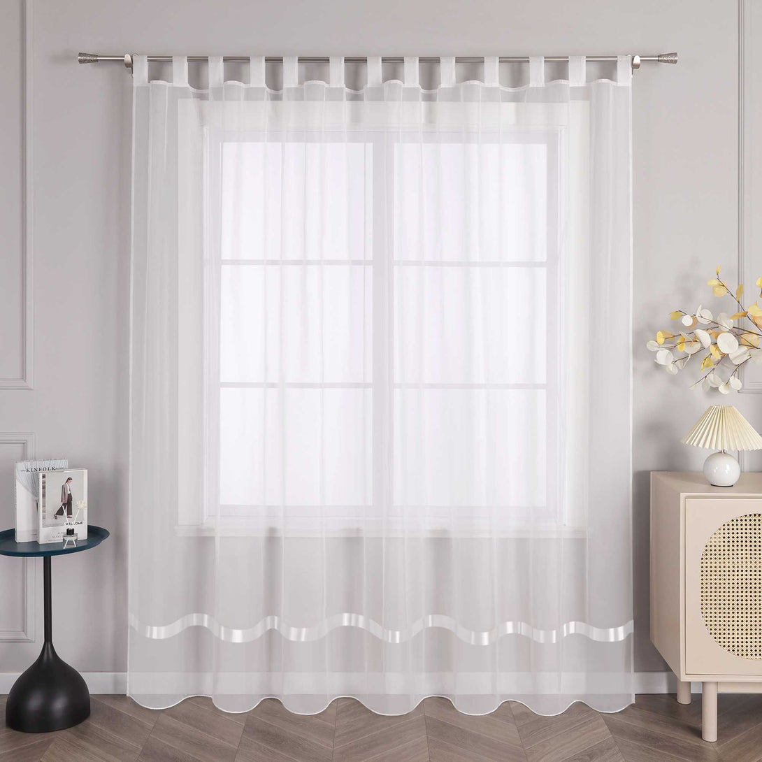 An einem Fenster hängt ein Vorhang mit Schlaufen, und am oberen Ende des Vorhangs befindet sich eine Metallstange, durch die die Schlaufen geführt sind, um den Vorhang an seinem Platz zu halten. Auf der linken Seite des Fensters steht ein kleiner schwarzer runder Tisch, auf dem einige Gegenstände stehen. Rechts vom Fenster steht ein heller Schrank mit einer Lampe mit hellem Schirm und einem Strauß dekorativer Blumen.