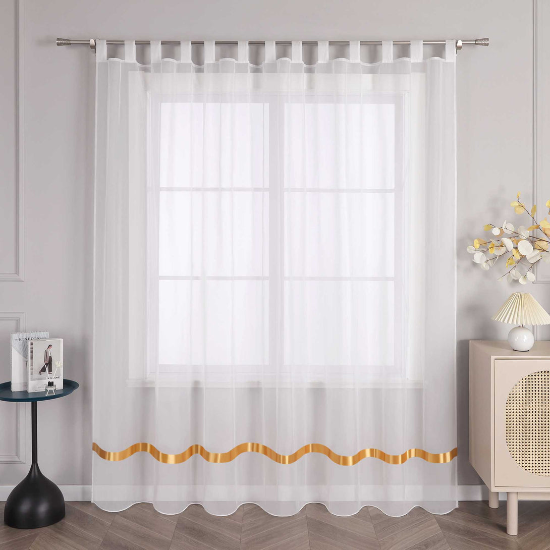An einem Fenster haengt ein weisser Vorhang mit orangefarbenen Satinbaendern und Schlaufen. Am oberen Ende fuehren die Schlaufen durch eine Metallstange, um den Vorhang an seinem Platz zu halten. Links vom Fenster steht ein kleiner schwarzer runder Tisch mit einigen Gegenstaenden. Rechts daneben befindet sich ein heller Schrank mit einer Lampe mit hellem Schirm und einem Strauss dekorativer Blumen.