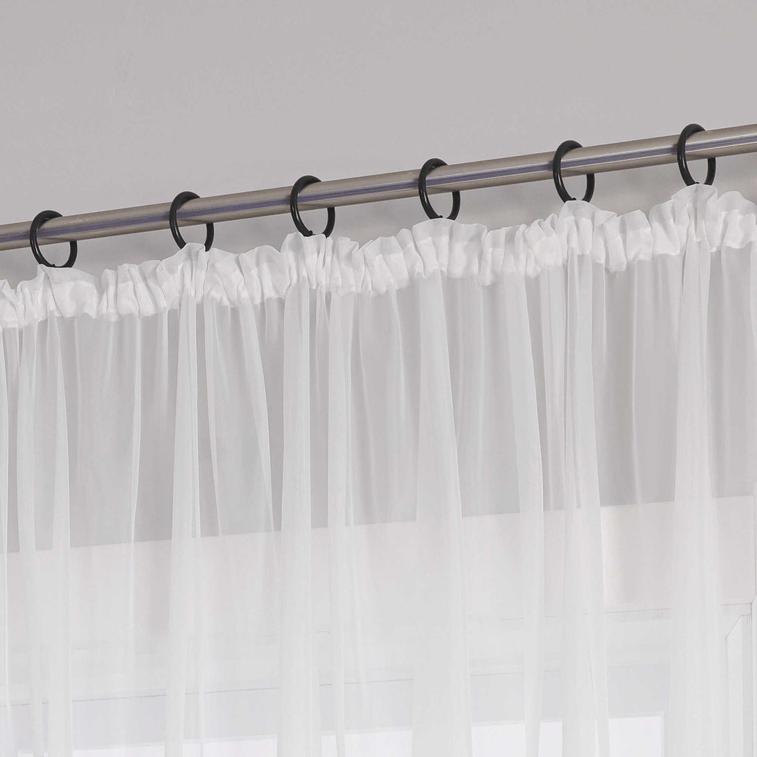 Eine Metallgardinenstange mit schwarzen Ringen, an denen ein weißer Vorhang mit Kräuseln aus transparentem Stoff aufgehängt ist. Der Vorhang hat am oberen Ende ein gerafftes Design.