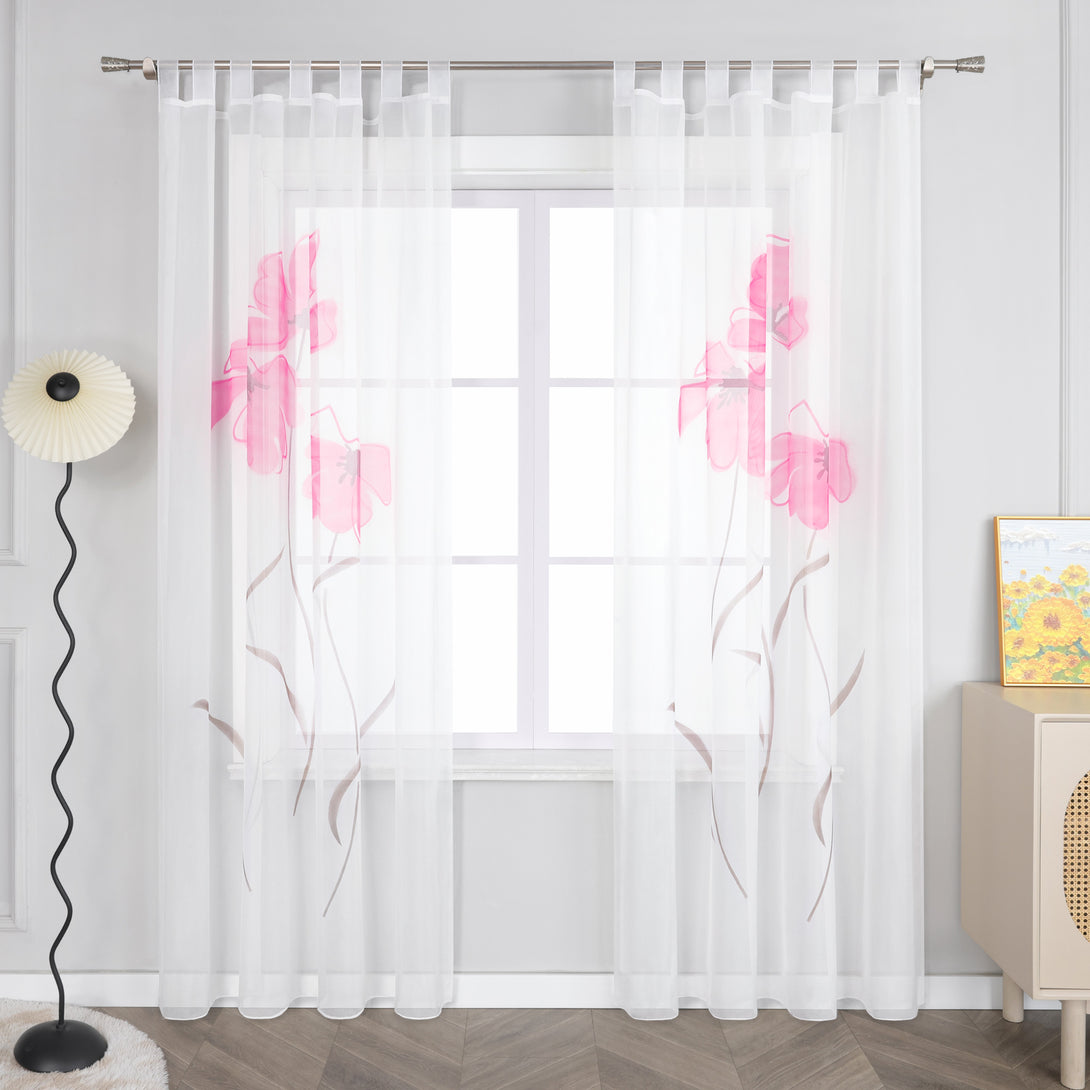 Das Bild zeigt einen weißen Vorhang, der an einem Fenster hängt, mit einem Muster aus rosa Blumen und braunen Zweigen. Der Vorhang ist mit Schlaufen an einer Metallstange befestigt. Neben dem Fenster steht eine Stehlampe mit einem schwarzen, gebogenen Stab und einem weißen, fächerförmigen Lampenschirm. Daneben befindet sich ein heller Schrank, auf dem ein Bild steht.