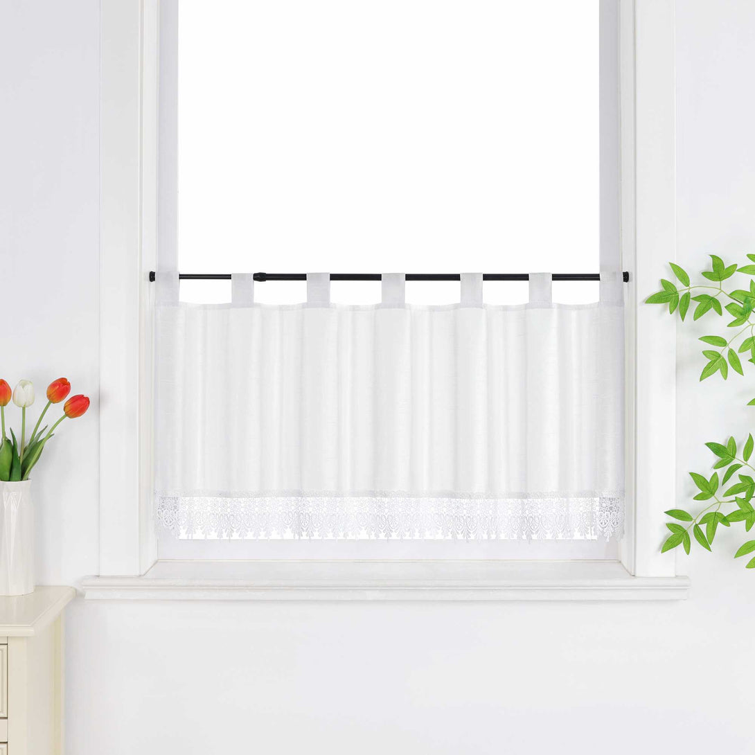 Weiße Scheibengardine hängt vor einem Fenster mit weißer Wand. Daneben sorgen rote Blumen, grüne Blätter und eine Vase für eine frische und dekorative Note.