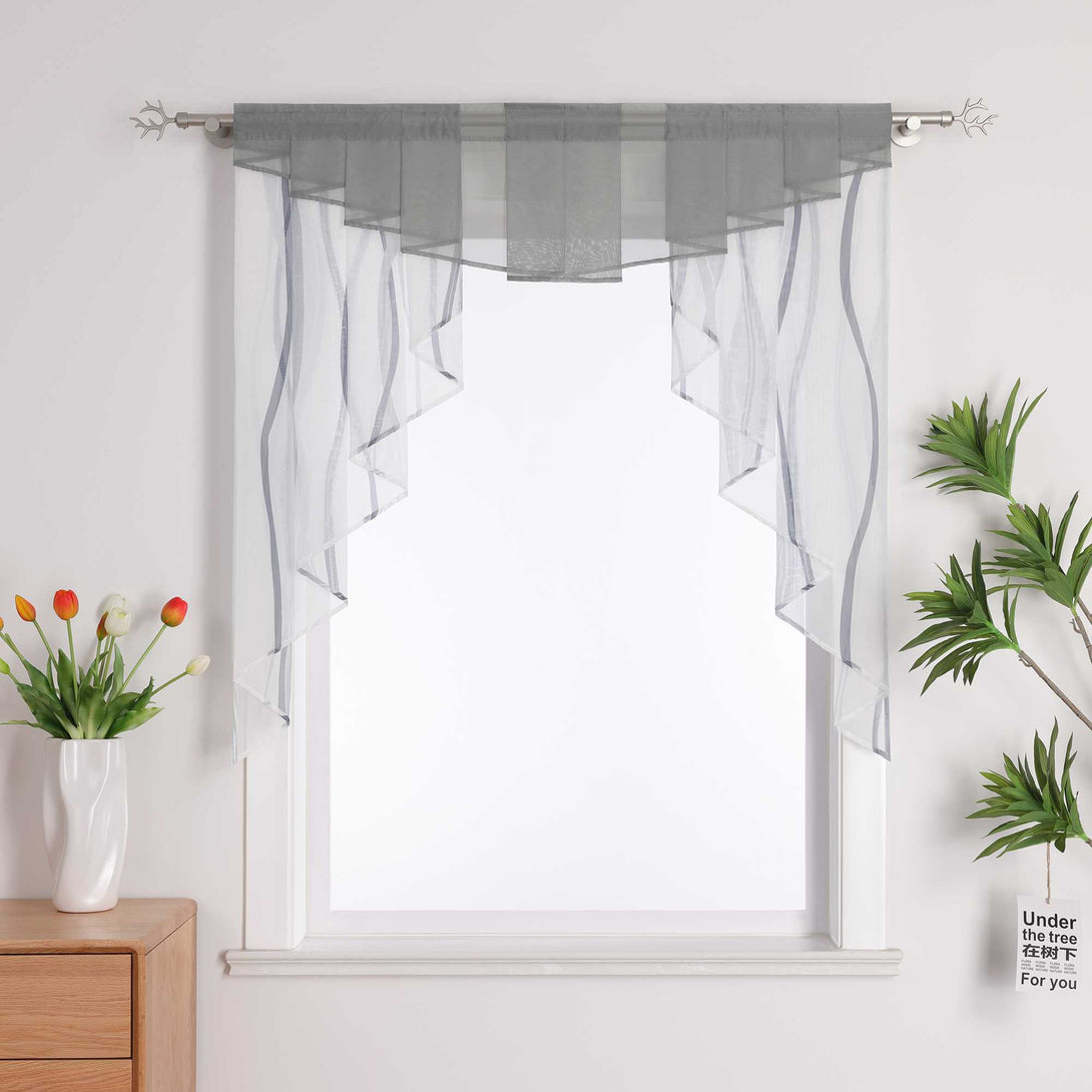 An einem Fenster hängt graue Gardine, daneben steht eine weiße Vase mit Blumen und eine grüne Pflanze.