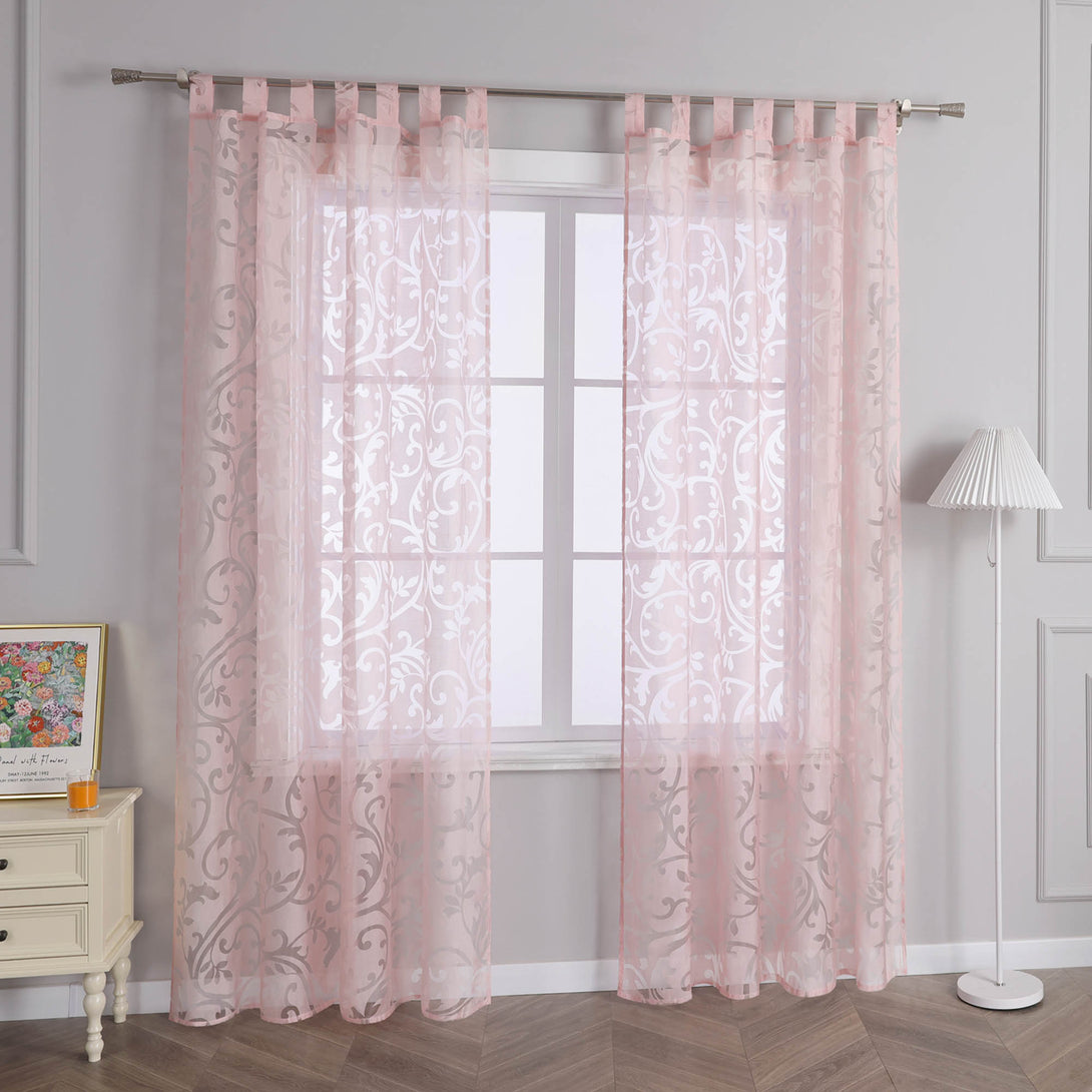 Das Bild zeigt eine Innenraumszene mit einem Fenster, an dem ein rosa, durchsichtiger Vorhang mit Blumenmuster hängt, der eine gute Lichtdurchlässigkeit bietet. Neben dem Fenster steht ein heller Schrank, auf dem ein dekoratives Bild und kleine Objekte platziert sind. In der Nähe steht eine weiße Stehlampe, die eine warme und sanfte Atmosphäre im Raum schafft.