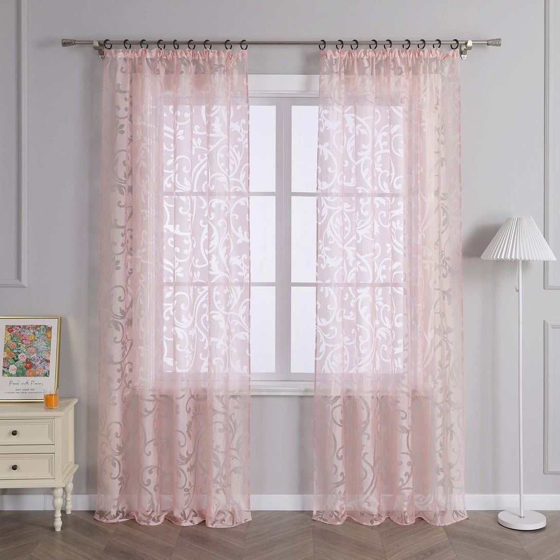 Das Bild zeigt ein Fenster, an dem ein rosa, durchsichtiger Vorhang mit Blumenmuster hängt. Der Vorhang hat eine gute Lichtdurchlässigkeit und wird durch Metallringe an einer Metallstange aufgehängt. Neben dem Fenster steht ein helles Regal, auf dem ein buntes Dekorationsbild und ein orangefarbenes kleines Objekt platziert sind. In der Nähe steht eine weiße Stehlampe, die eine warme und sanfte Atmosphäre im Raum schafft.