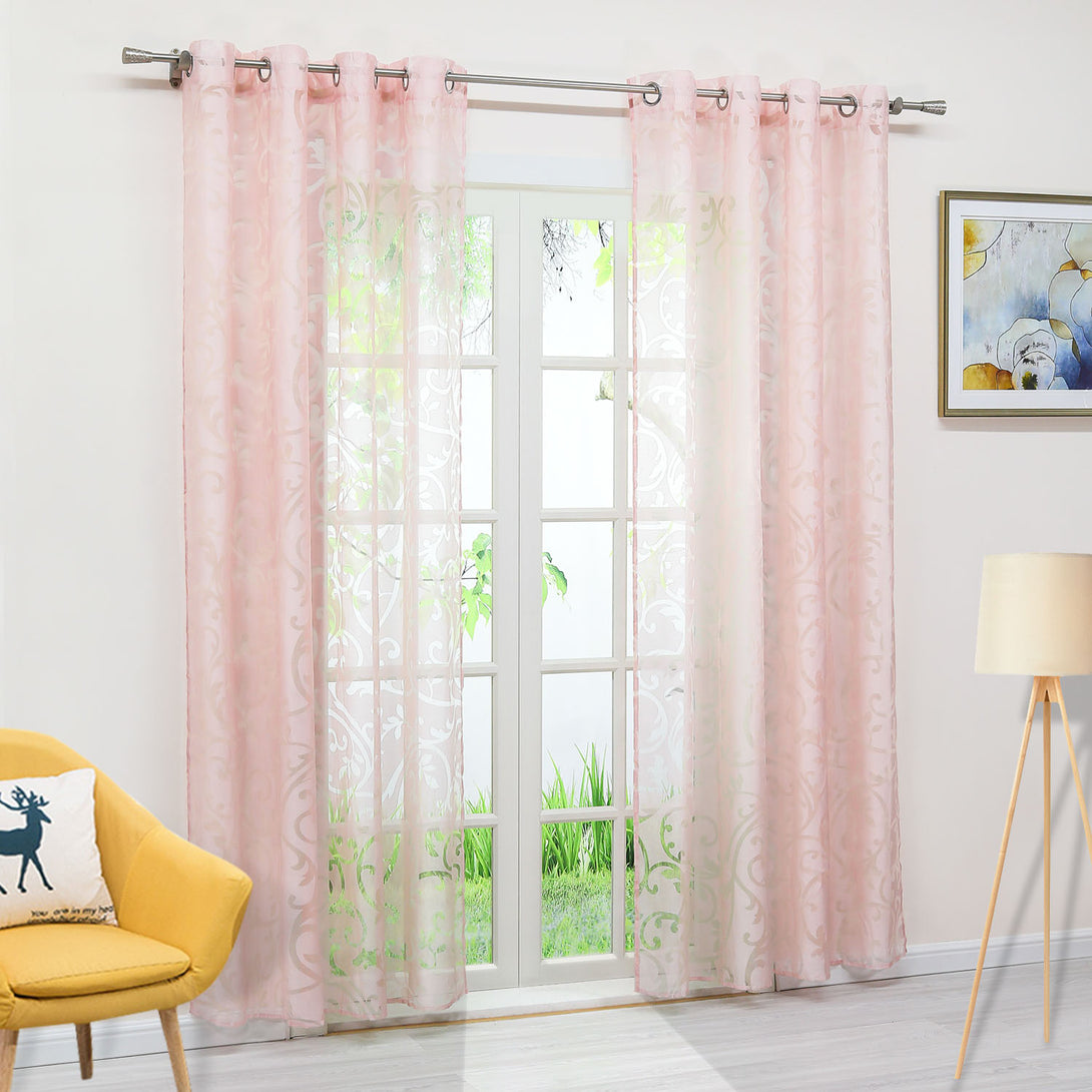 Das Bild zeigt ein Fenster in einem Innenraum, an dem ein rosa, durchsichtiger Vorhang mit Blumenmuster hängt, der eine gute Lichtdurchlässigkeit bietet. Der Vorhang ist mit Metallringen an einer Metallstange aufgehängt. Neben dem Fenster steht ein gelber Stuhl, auf dem ein gemustertes Kissen liegt, und daneben eine weiße Stehlampe. An der Wand hängt ein dekoratives Gemälde. Durch das Fenster ist ein grünes Außenbild sichtbar. Die gesamte Szene schafft eine warme und gemütliche Atmosphäre im Raum.