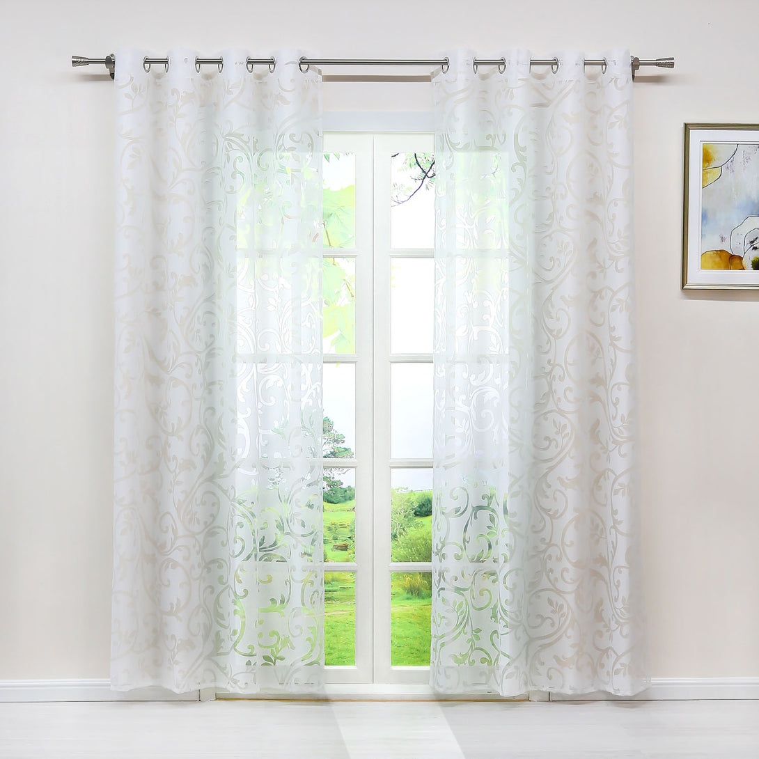 Dies ist eine Innenraumszene, in der an einem Fenster ein weißer, durchsichtiger Vorhang mit Blumenmuster hängt. Durch den Vorhang ist die grüne Landschaft draußen sichtbar. Der Vorhang wird durch Metallringe an einer Metallstange aufgehängt. An der Wand neben dem Fenster hängt ein dekoratives Bild.